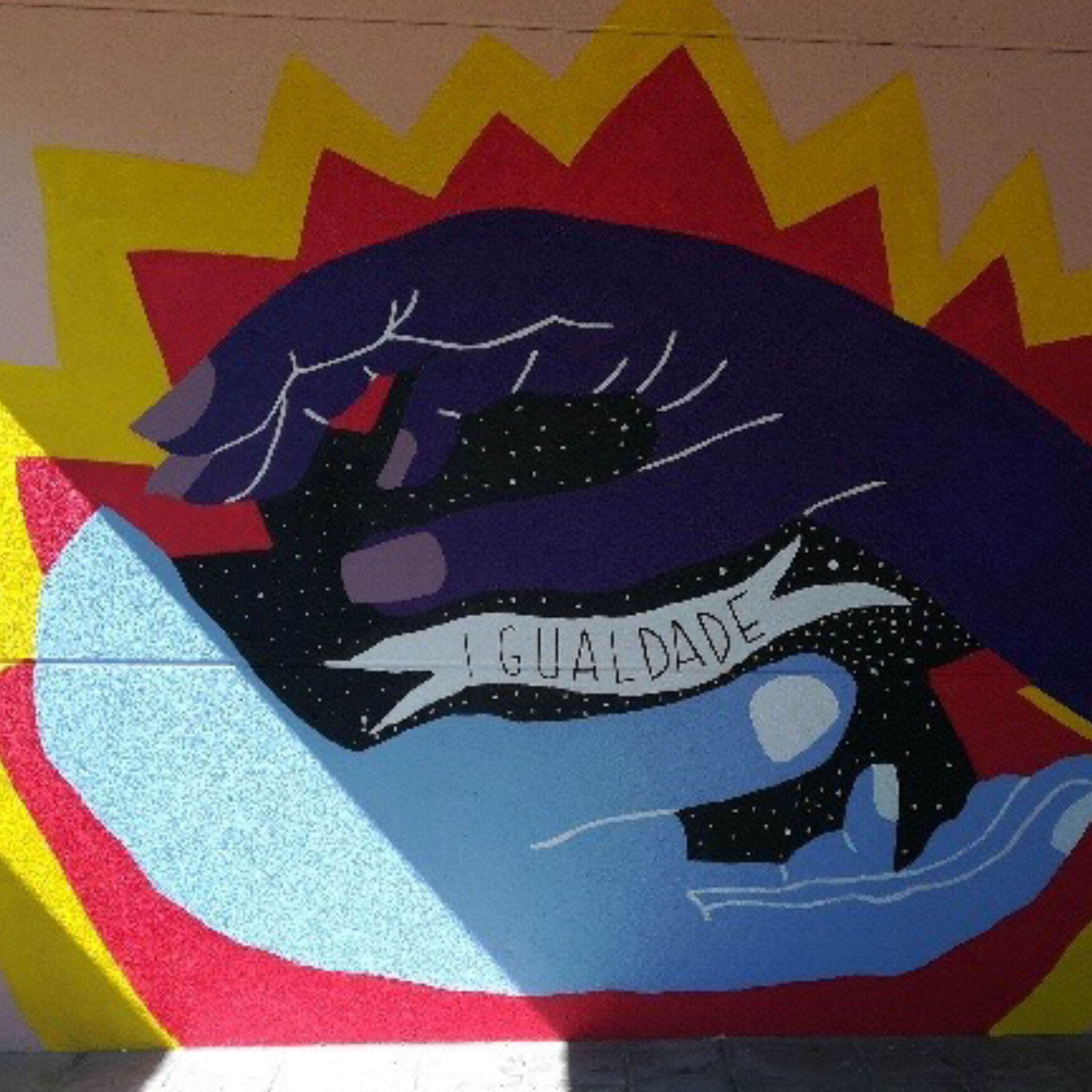 Mural feito na fachada dunha escola cunhas mans que case se tocan co texto igualdade.